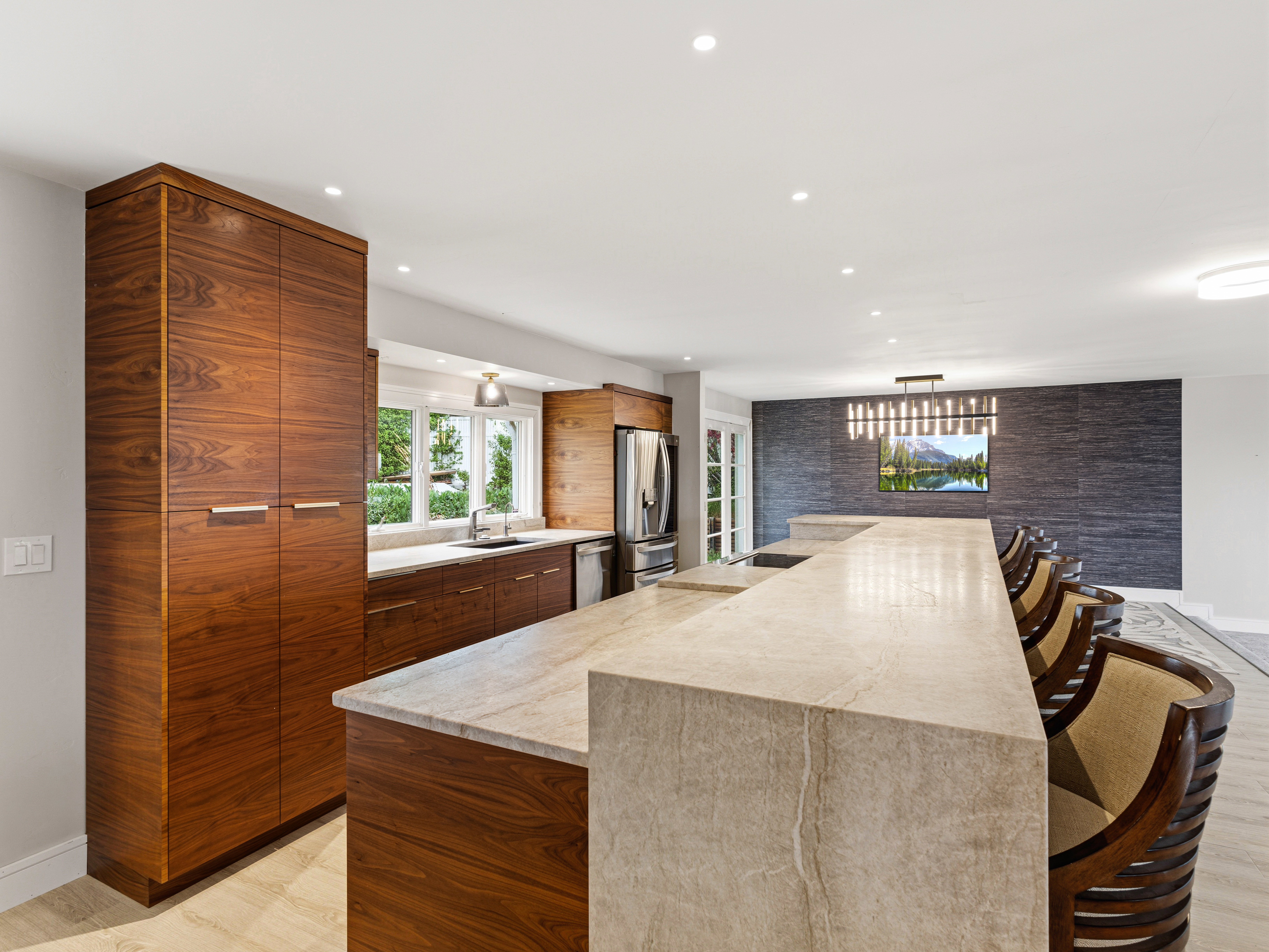 Open-concept kitchen featuring extensive wood-finish cabinetry, a large stone slab island, recessed lighting, and a stainless steel refrigerator