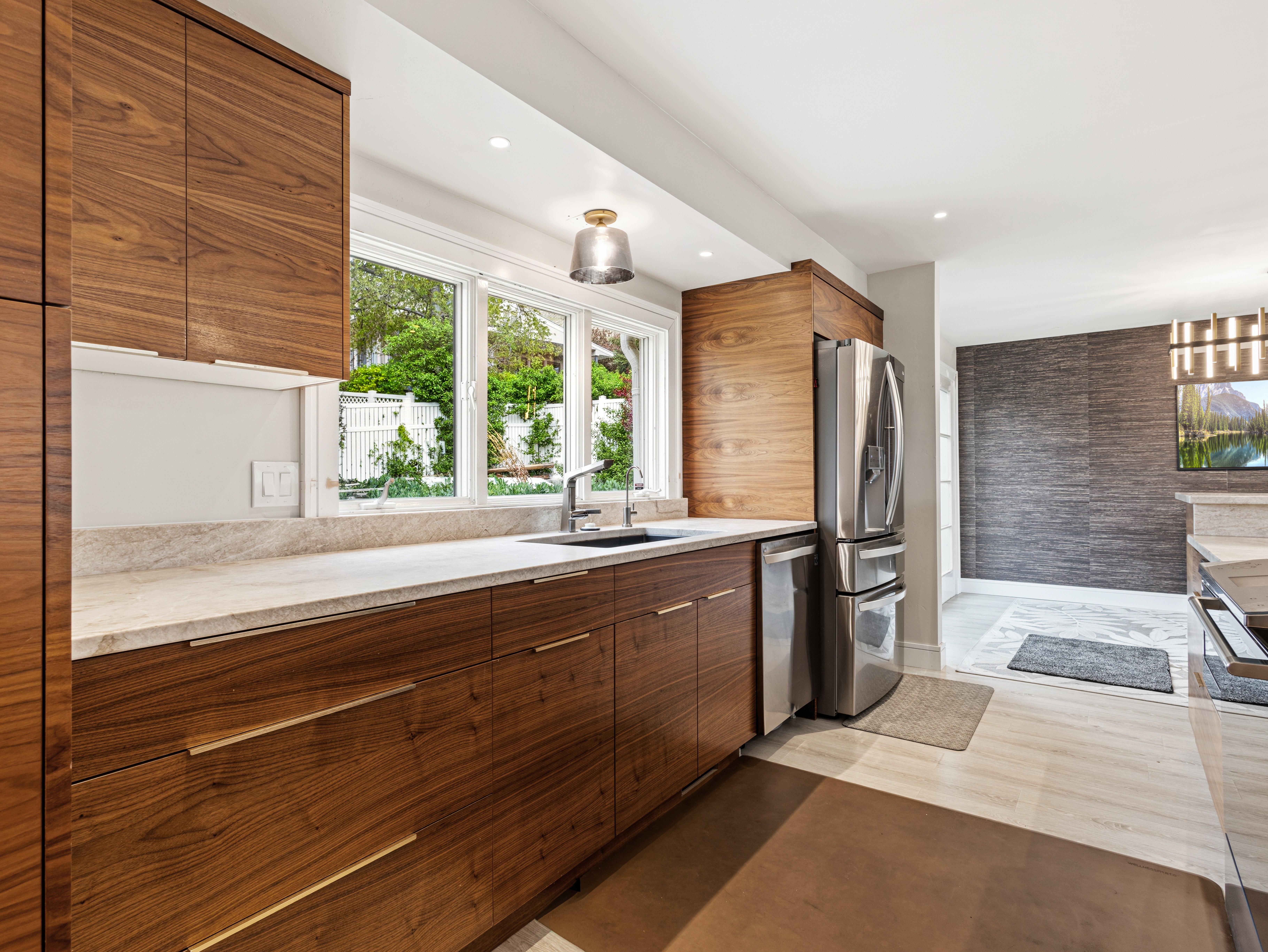 Modern kitchen featuring wood-finish cabinetry, light stone countertops, and stainless steel appliances including a refrigerator and dishwasher