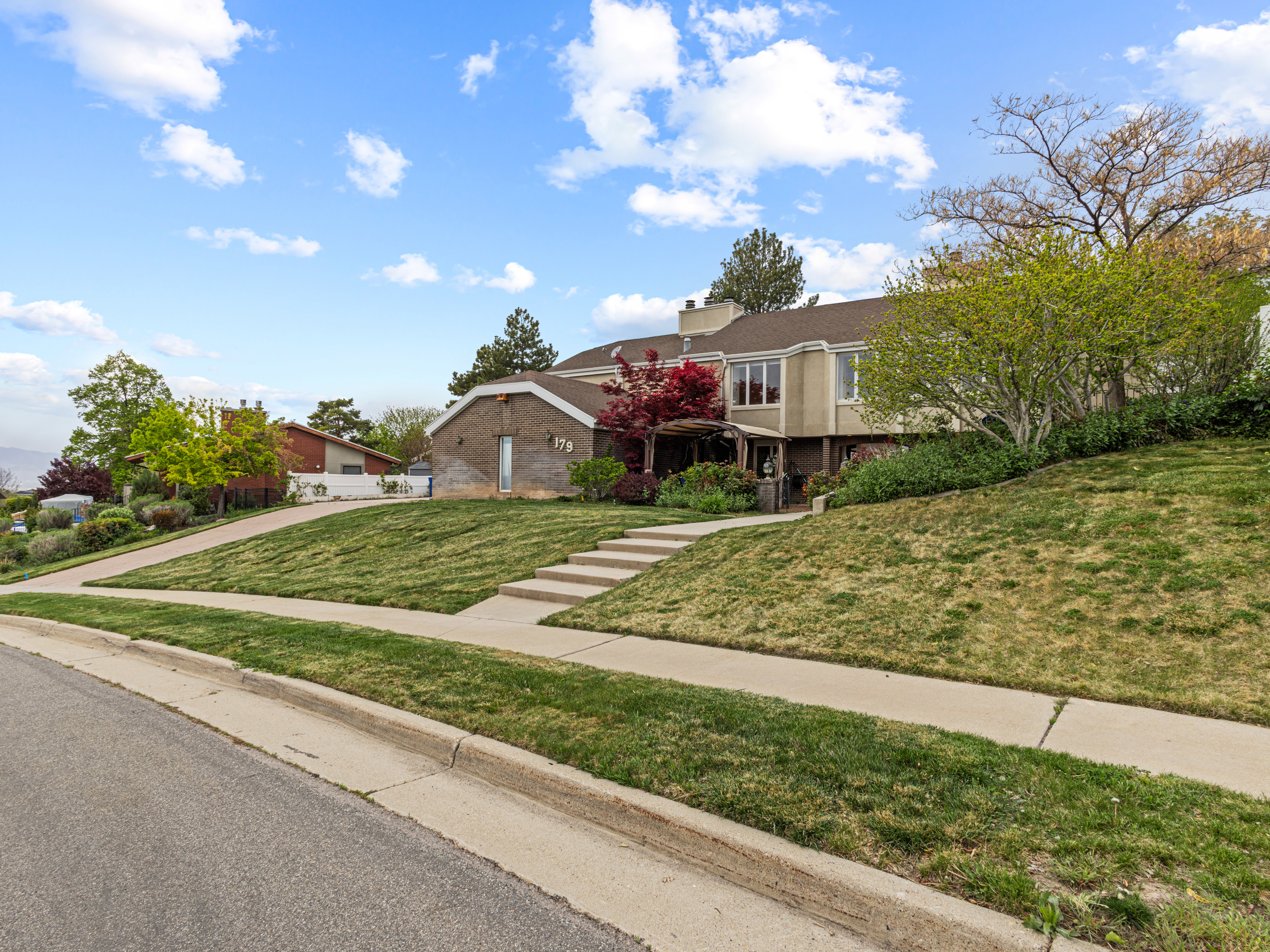 Multi-level residence featuring a stucco and brick exterior, mature landscaping, and a terraced front yard with concrete steps
