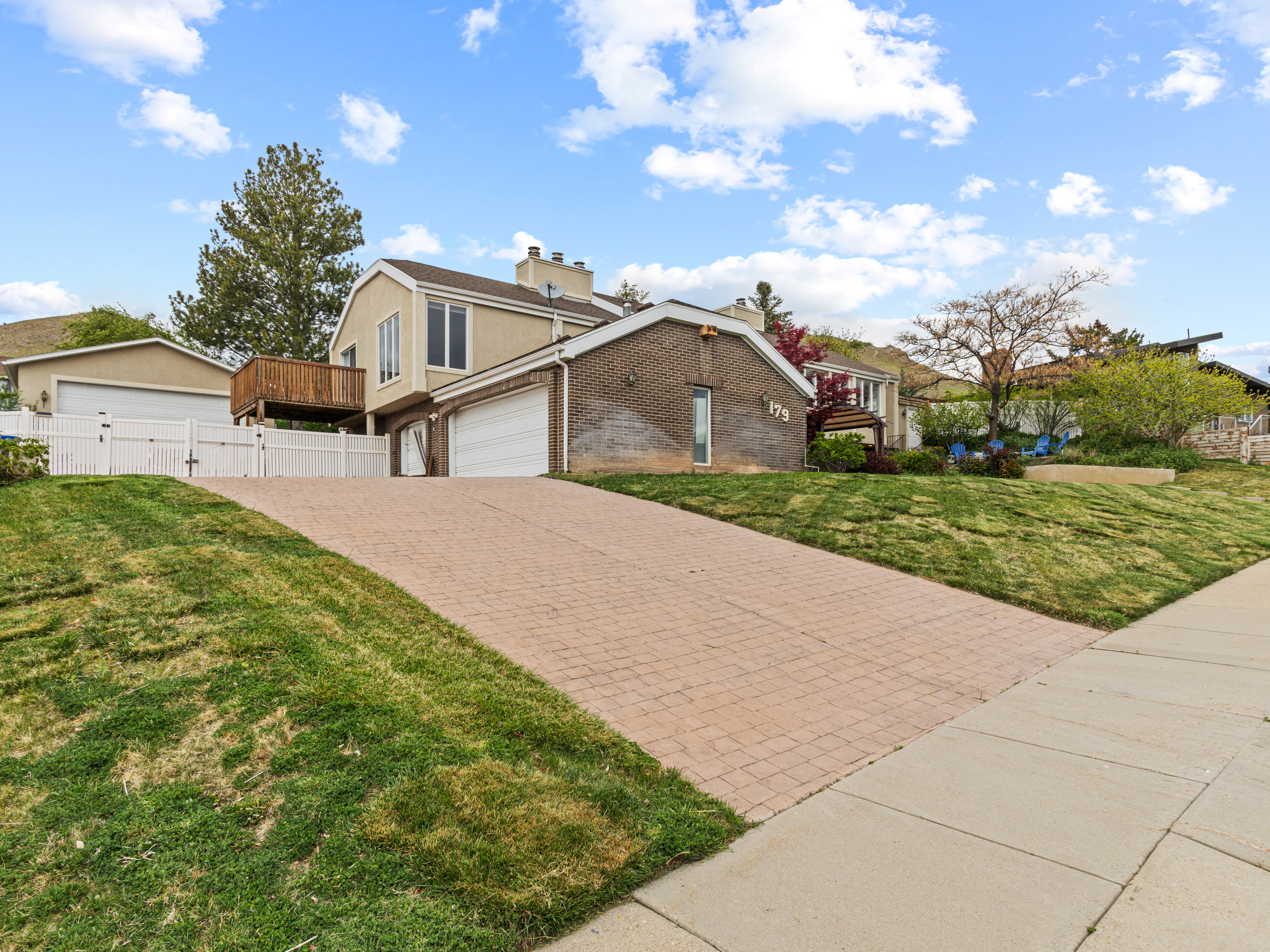 Residence featuring a multi-tone exterior, an attached garage, a private wood deck, and a paver driveway