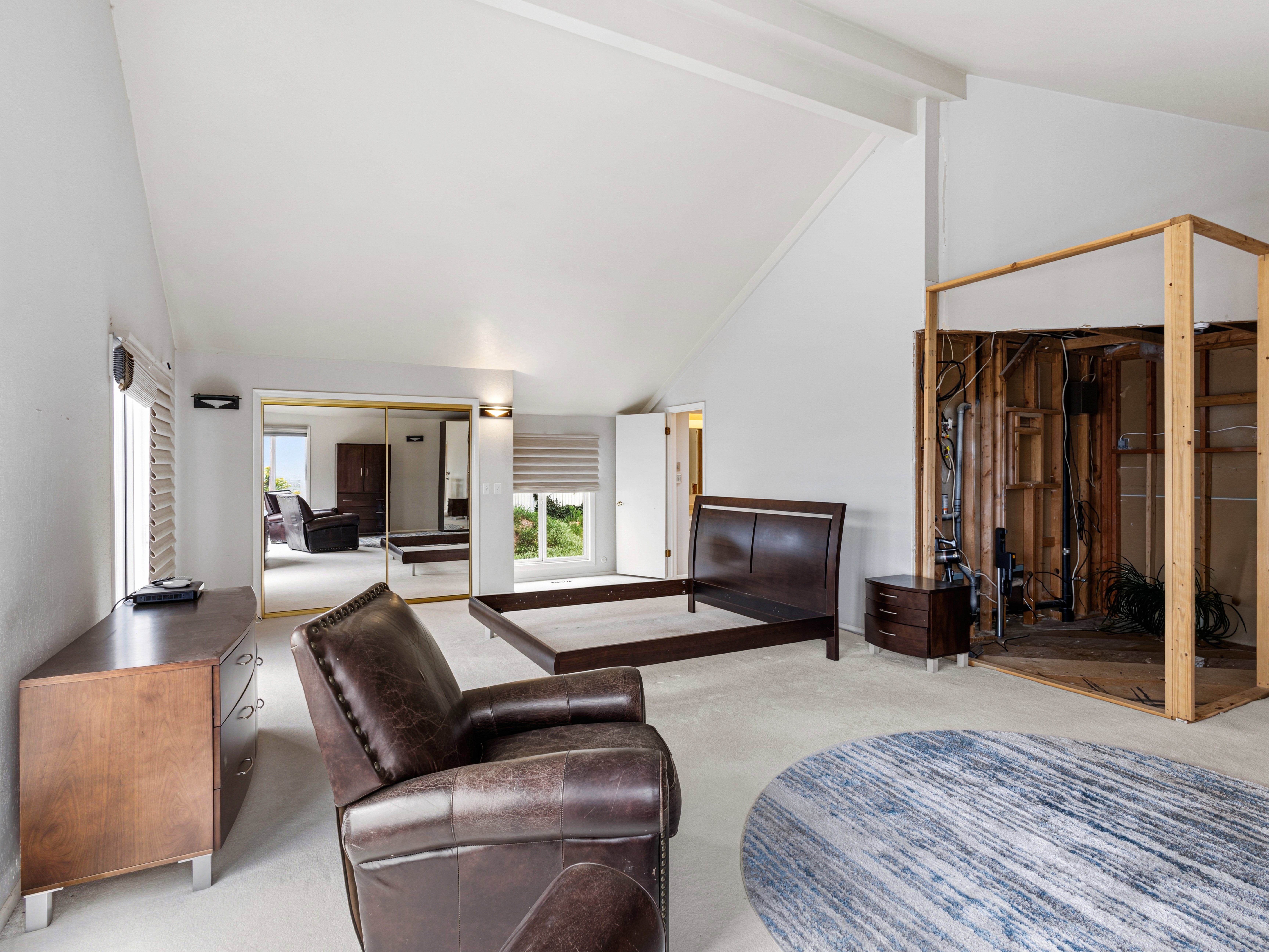 Vaulted ceilings enhance this spacious room, featuring white walls, carpeting, and a mirrored closet
