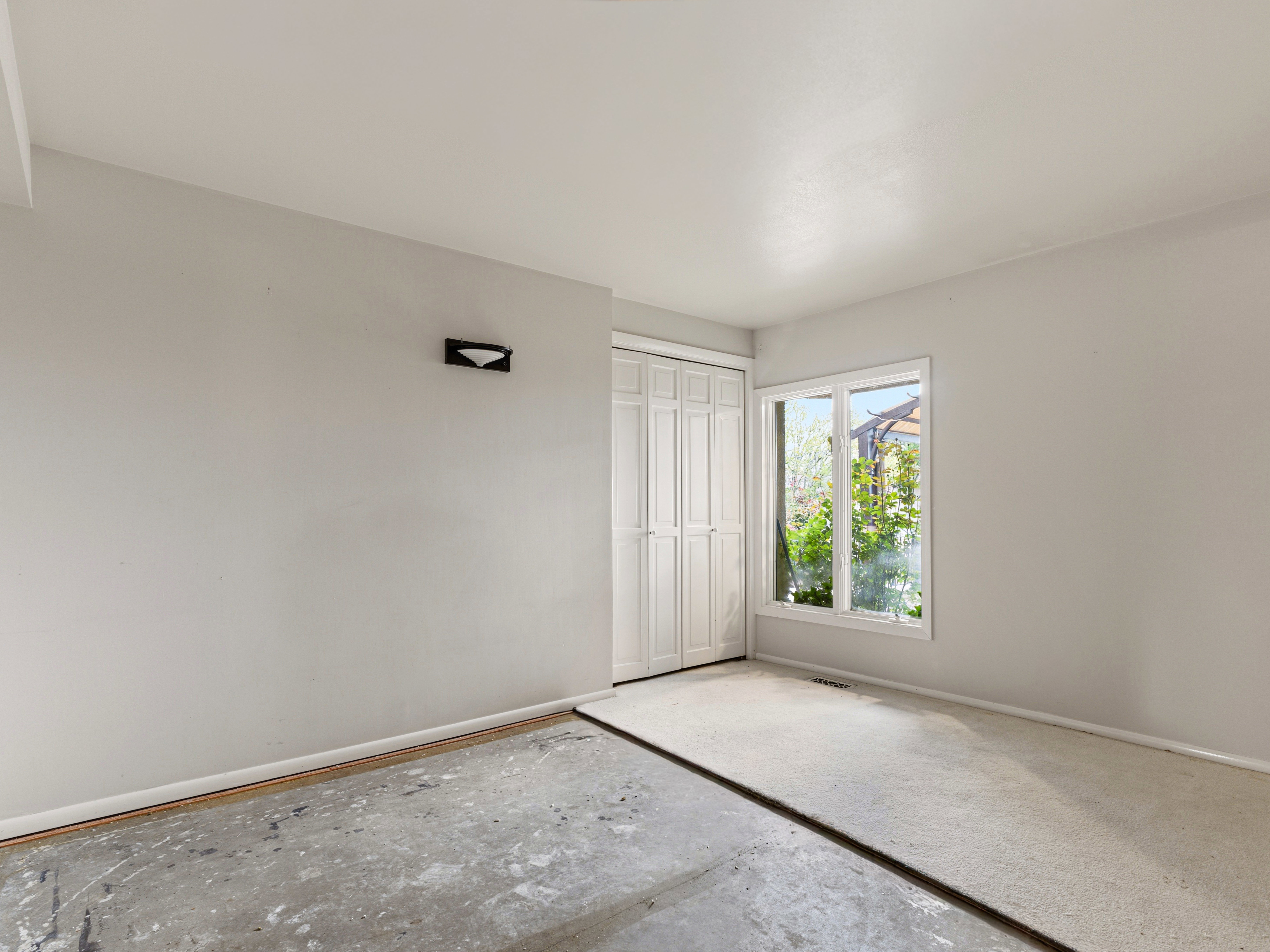 Room featuring a white-framed window, white walls, and a combination of concrete and partial carpeting