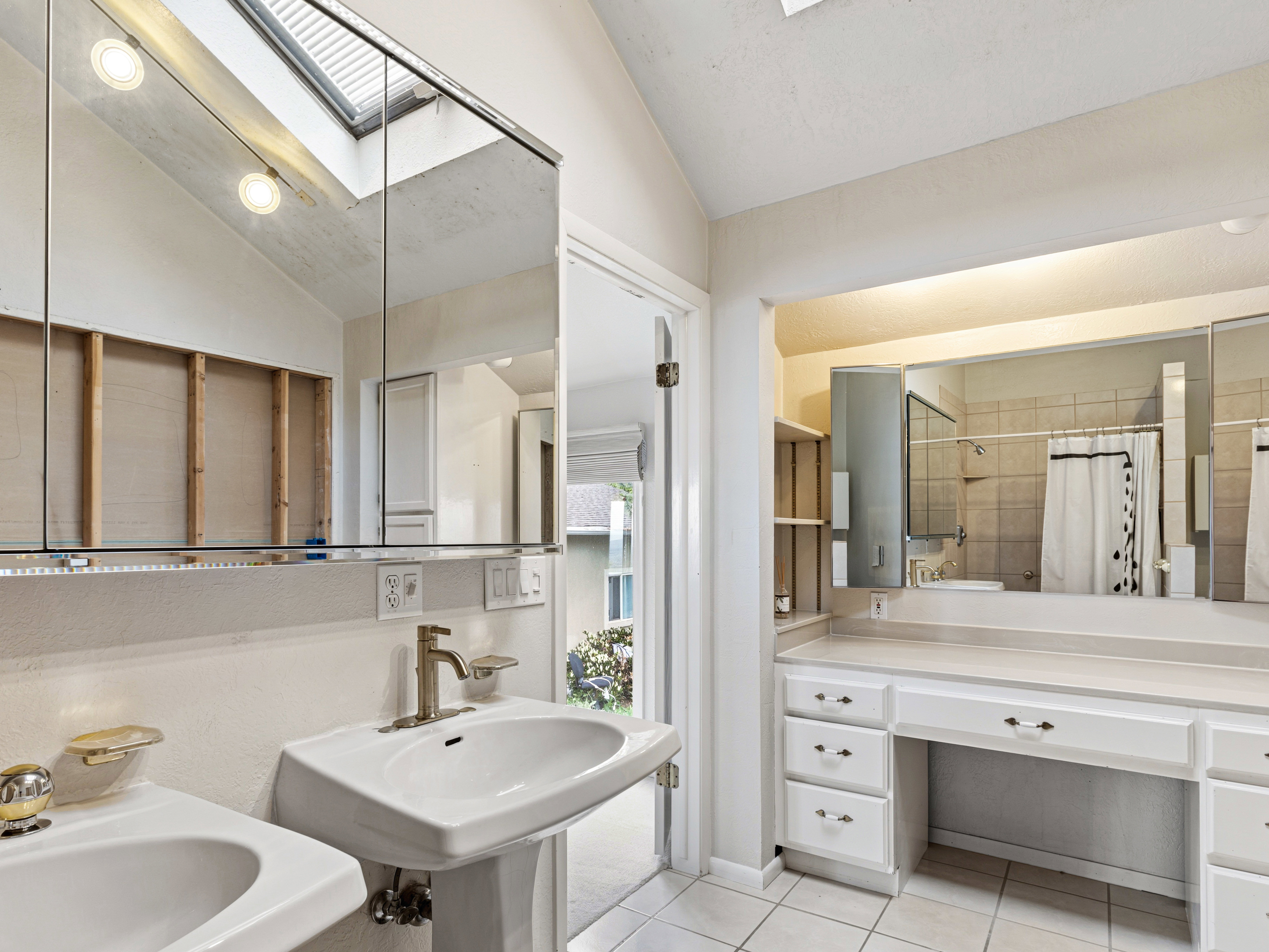 Bathroom featuring a pedestal sink, vanity with integrated cabinetry, tile flooring, and a skylight