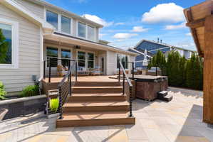 Expansive outdoor living area featuring a multi-level deck with cable railing, a built-in hot tub, and a large paver patio
