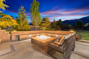 Paver patio with a built-in fire pit, integrated bench seating, retaining walls, and ambient lighting