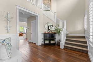 Entry foyer featuring wood-finish flooring, a carpeted staircase with white balusters, and a wainscoting accent wall
