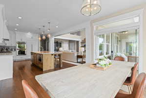 Kitchen and dining area featuring hardwood flooring, a central island with integrated appliances, white cabinetry, double wall ovens, and sliding glass doors to an outdoor area