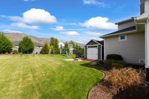 Expansive backyard featuring a large green lawn, a dedicated play area, a storage shed with double doors, a paved patio, and mountain scenery
