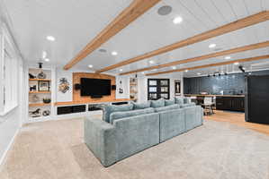 Spacious entertainment area featuring a built-in media center with wood accent wall, recessed lighting, exposed ceiling beams, built-in shelving, and a wet bar with dark subway tile backsplash and hardwood flooring