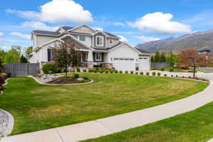 Expansive front lawn with manicured landscaping, a three-car garage, partial stone facade, and a mountain backdrop
