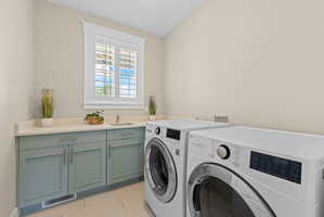 Dedicated laundry space featuring a built-in sink, light-toned countertop, and blue-gray cabinetry with silver hardware