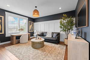 Spacious room featuring rich wood-finish flooring, white plantation shutters, board and batten wall detailing, recessed lighting, and a woven pendant light fixture