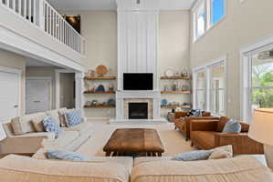 Spacious living area featuring a double-height ceiling, an integrated fireplace with a stone surround, and a white mantel