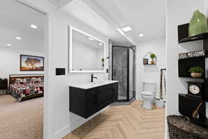 Modern bathroom featuring herringbone wood-finish flooring, a wall-mounted vanity with a rectangular sink, a lit mirror, and a glass-enclosed shower