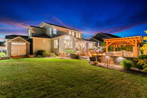 Expansive backyard featuring a manicured lawn, a multi-level deck with built-in hot tub, and a pergola-covered outdoor kitchen with stone detailing