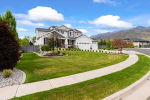 Contemporary residence featuring a multi-tone exterior, attached multi-car garage, manicured lawn, paved driveway, and mature landscaping