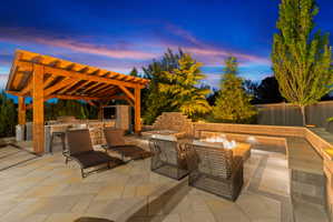 Expansive paver patio featuring a timber-framed outdoor kitchen with integrated appliances, a built-in fire pit, and tiered landscaping with perimeter lighting
