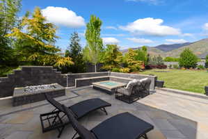 Expansive hardscaped patio featuring a built-in fire pit with decorative glass, a stone-block retaining wall, and integrated bench seating