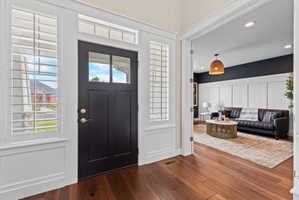Entryway featuring a dark wood-finish door with upper glass panels, side light windows with white plantation shutters, and rich wood-finish flooring