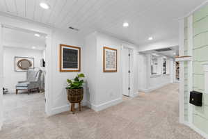 Recessed lighting illuminates a hallway with light-toned carpeting and white walls