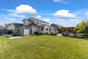 Expansive backyard featuring a lush lawn, a detached shed with a white garage door, and a multi-level patio with a wooden pergola