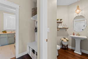 Powder room featuring a pedestal sink, round mirror, and a decorative chandelier, with wood-finish flooring