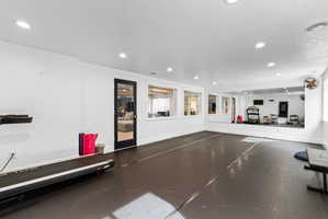 Expansive recreational space featuring dark flooring, recessed lighting, a full-wall mirror, and multiple window openings with wood trim
