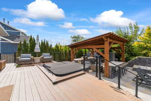 Expansive outdoor living area featuring a multi-level composite deck, built-in hot tub, and a pergola-covered patio with a gas fire pit