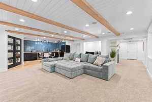 Spacious lower-level entertainment area featuring exposed wood ceiling beams, recessed lighting, and light-tone carpeting