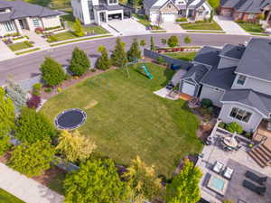 Expansive backyard featuring a large manicured lawn, established perimeter trees, a multi-level patio with a fire pit, and a wooden deck