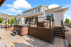 Expansive outdoor living area featuring a multi-level deck with black railing, integrated hot tub, and paver patio