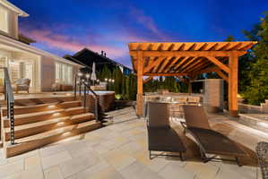 Expansive outdoor living area featuring a wood pergola with an outdoor kitchen, a built-in hot tub, and a multi-level composite deck with integrated stair lighting and cable railings
