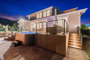 Tiered patio with integrated spa, featuring a wood-finish exterior, stone paver base, covered deck, and exterior lighting