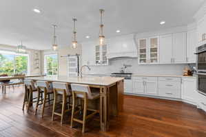 Gourmet kitchen with a large center island, white shaker cabinetry, stainless steel appliances, and wood-finish flooring