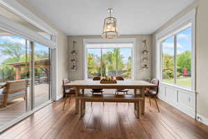 Spacious dining area featuring wood-finish flooring, a contemporary chandelier, and extensive natural light from multiple windows
