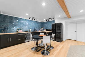 Modern kitchen area featuring a blue subway tile backsplash, dark cabinetry, and light wood-finish flooring