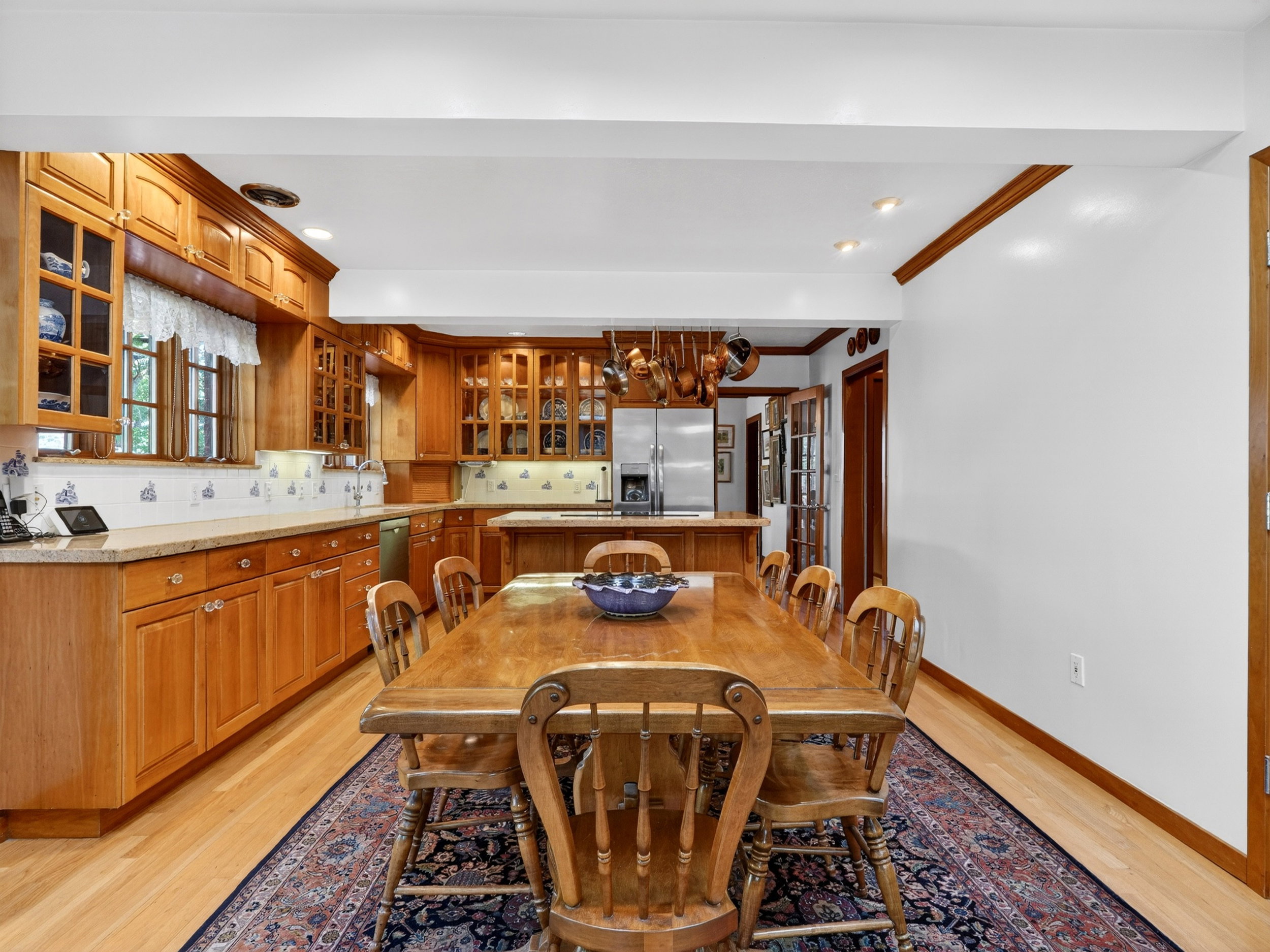 Open-concept kitchen and dining area featuring natural wood cabinetry, granite countertops, wood-finish flooring, recessed lighting, and a stainless steel refrigerator