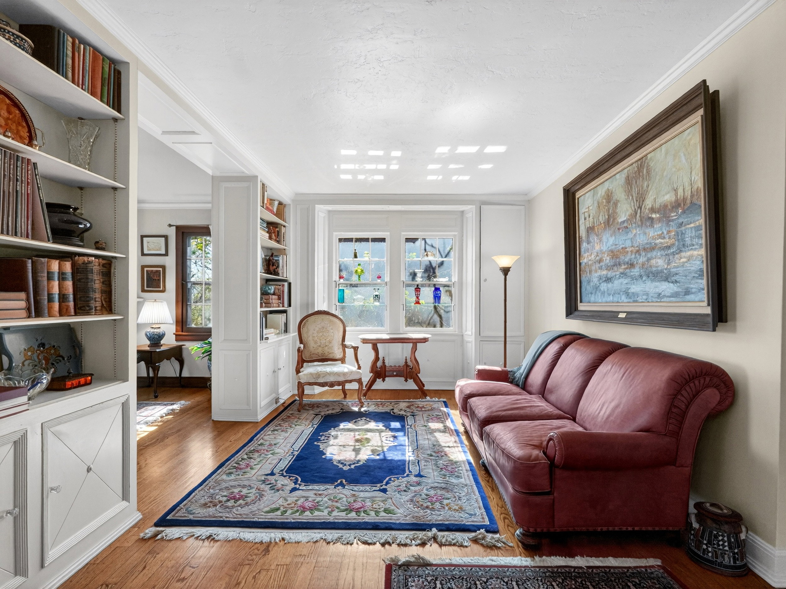 Hardwood flooring featuring built-in shelving, crown molding, and large windows with white trim