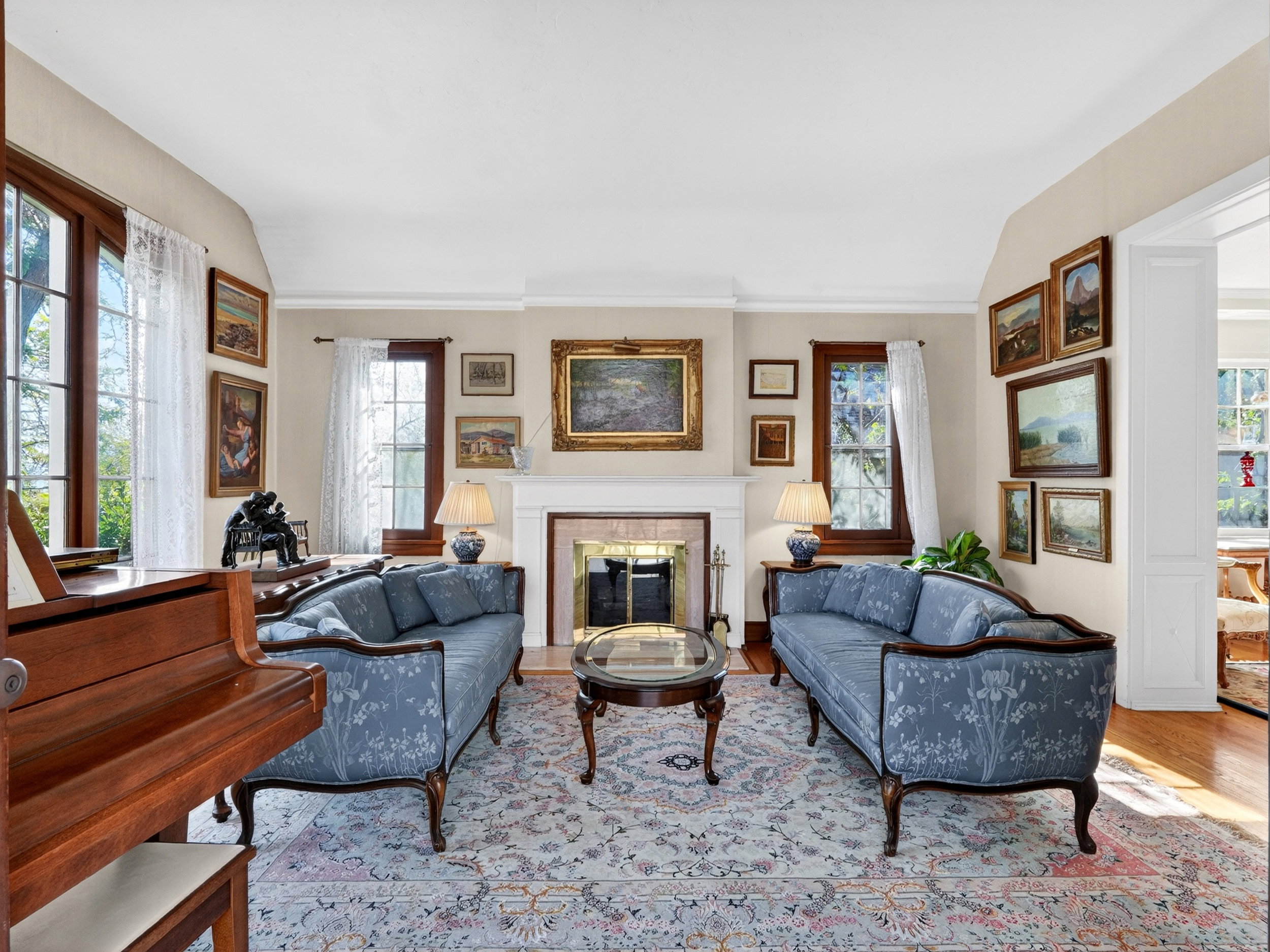 Living area featuring a fireplace with a stone surround, hardwood flooring, and multiple large windows with wood trim