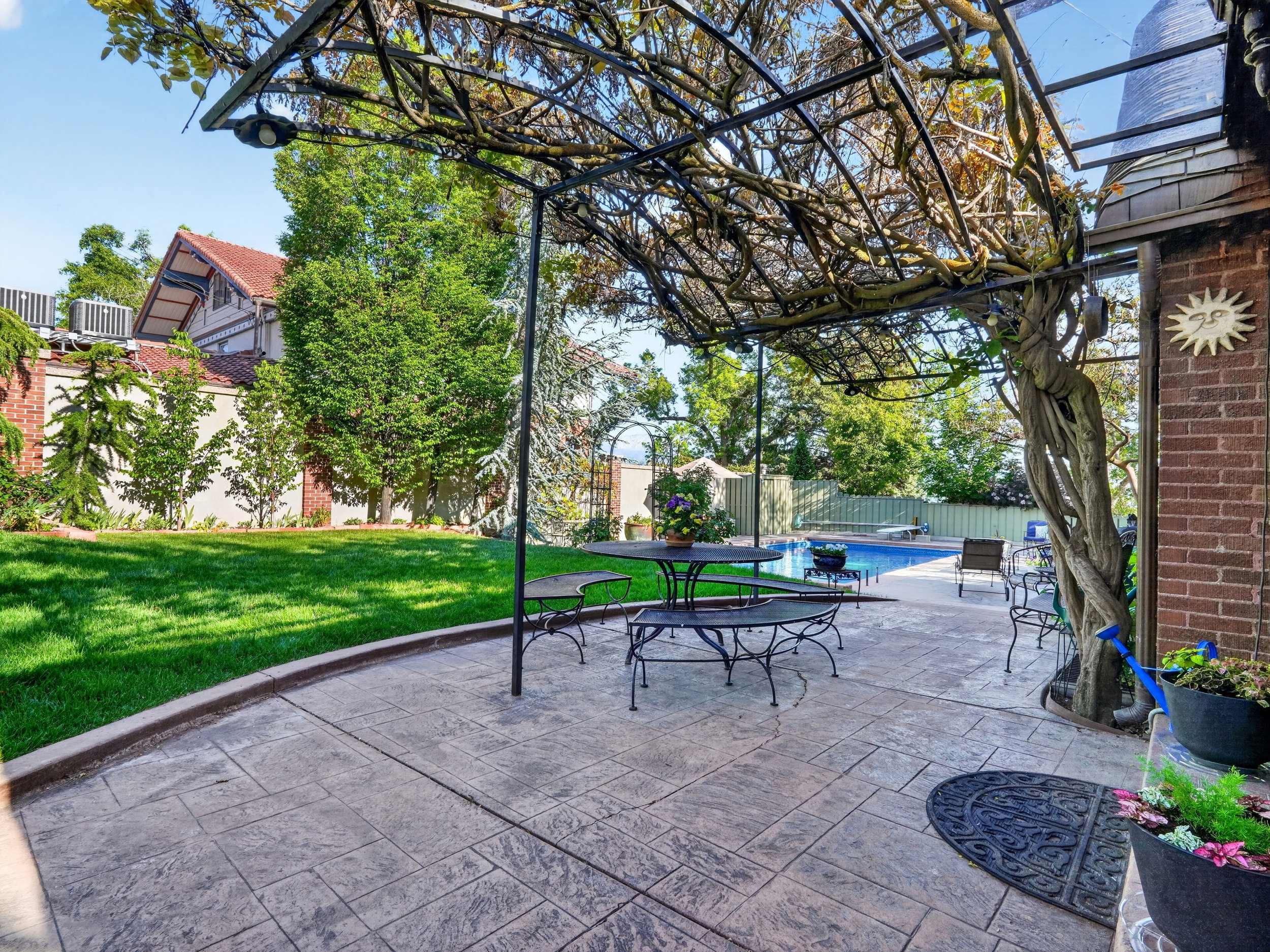 Stamped concrete patio with an overhead pergola featuring mature climbing vines