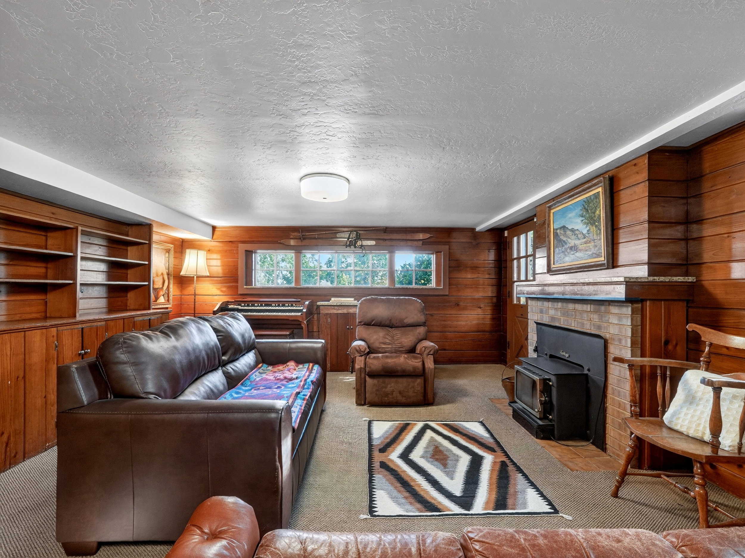 Basement Family room with built-in shelving, a brick fireplace with a black wood-burning stove.