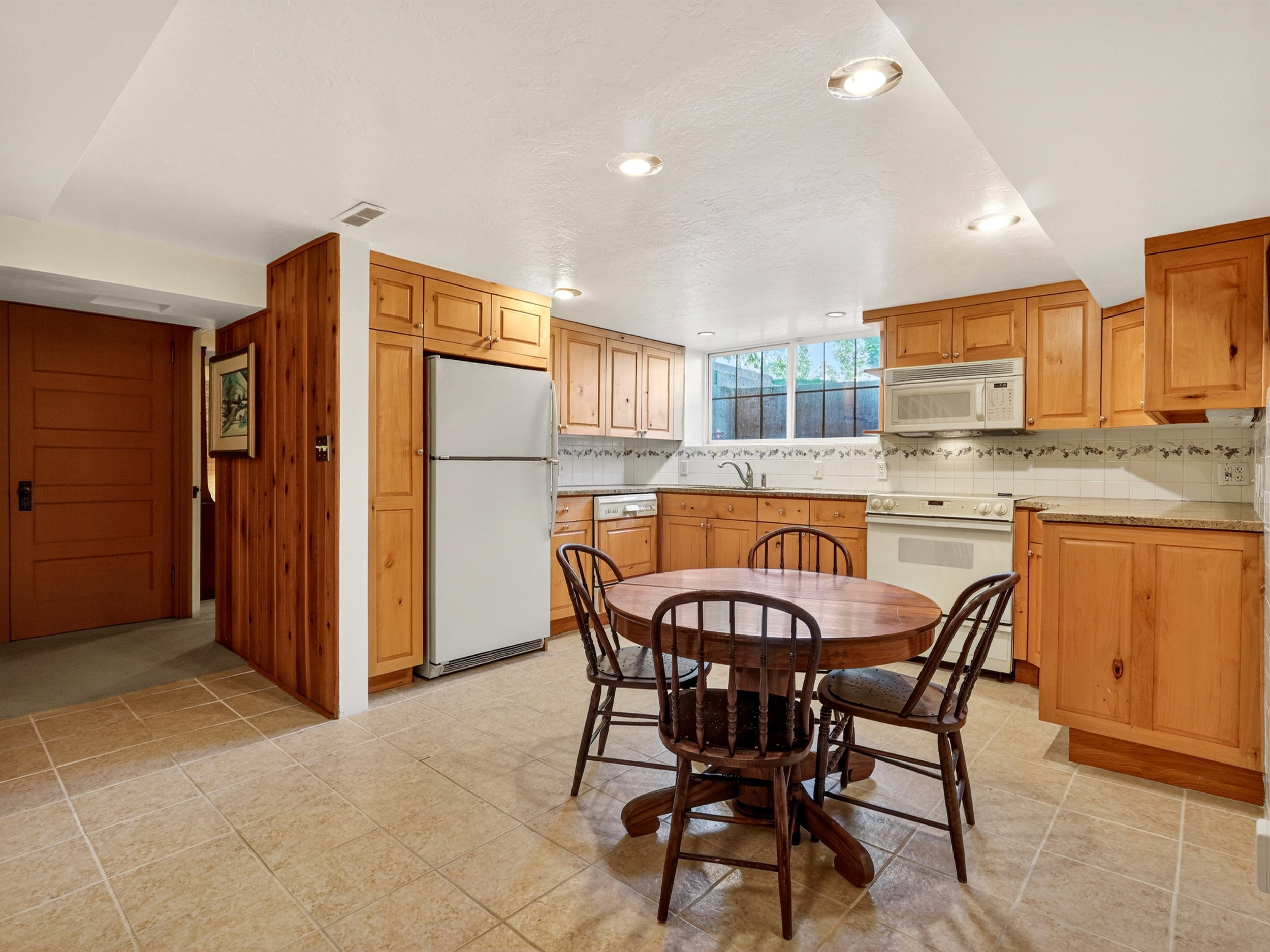 Basement Kitchen area featuring warm wood cabinetry, neutral tile flooring, recessed ceiling lighting, and a white appliance suite