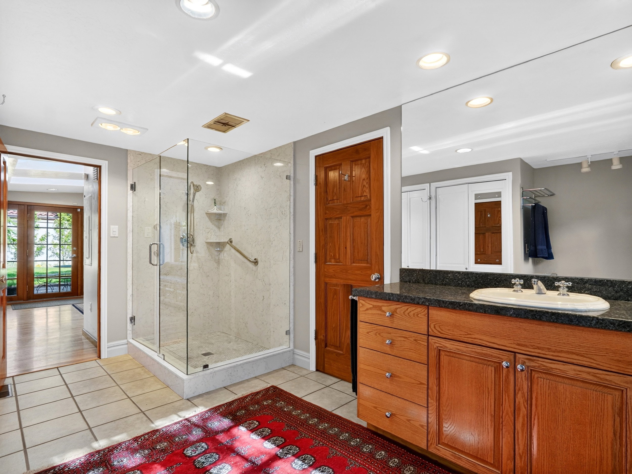 Bathroom featuring a glass-enclosed shower with grab bar, a wood-finish vanity with a vessel sink, granite countertop, and tile flooring
