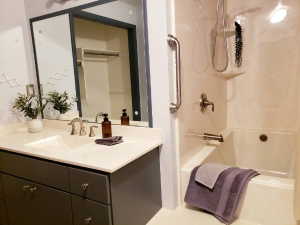 Bathroom featuring a built-in tub and shower combination with a grab bar, a vanity with an integrated sink, a light-toned countertop, and dual sliding mirrored doors