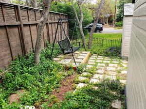 Fenced outdoor patio area featuring a paver stone walkway, mature trees, and established plantings