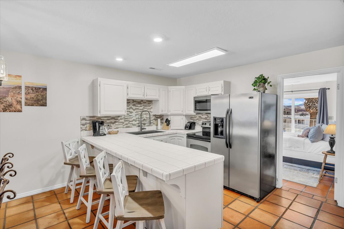Kitchen featuring white cabinetry, tile countertops, stainless steel appliances, a patterned tile backsplash, and terracotta-style floor tiles