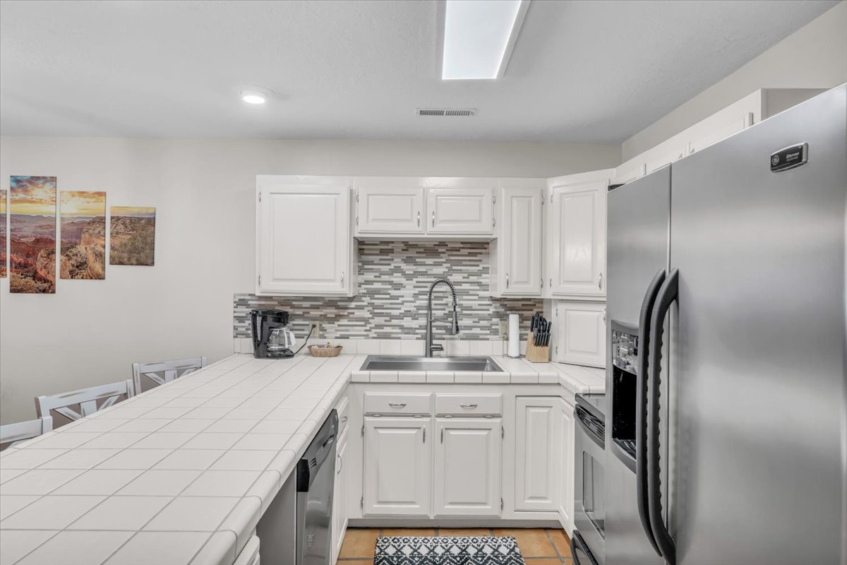 Kitchen featuring white cabinetry, a tiled countertop, and a mosaic tile backsplash