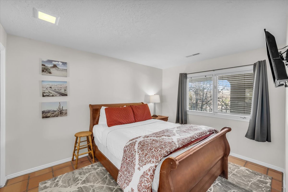 Bedroom featuring terra cotta tile flooring, a window with horizontal blinds, and a ceiling-mounted light fixture