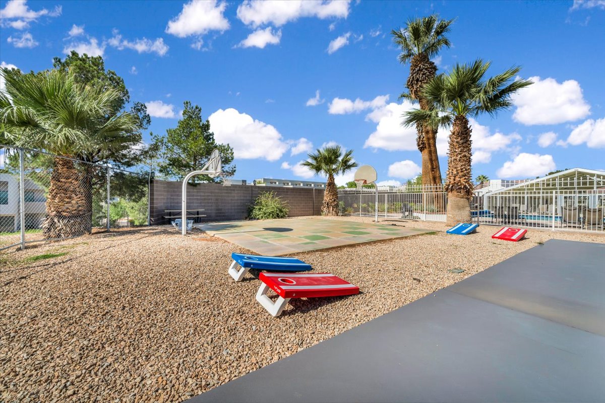 Outdoor recreation area featuring a basketball court, gravel landscaping, multiple palm trees, and a perimeter fence
