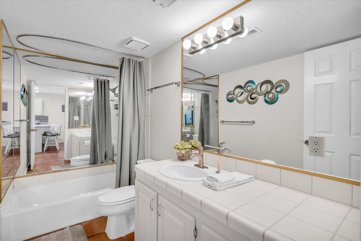 Bathroom featuring a full vanity with an integrated sink, white tiled countertop, and a large mirror with a brass-finish frame